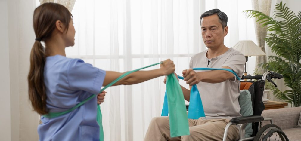 asian Japanese handicapped mature male doing resistance exercise on wheelchair with his nursing aide. they pull the stretch tape to make fists bump.
