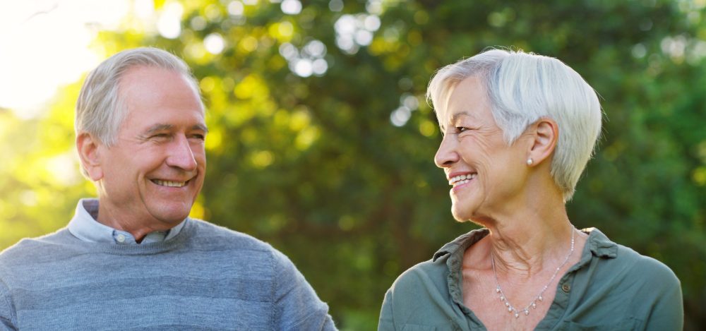 Senior couple, happy and love outdoor at a park with a smile, care and support for health and wellness. A elderly man and woman in nature for a walk, quality time and healthy marriage or retirement.